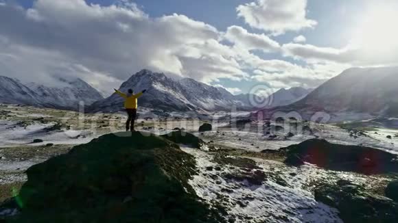 男子站在石峰上白雪皑皑的冬山山脉成就成功伸出双臂幸福史诗般的自然美景视频的预览图