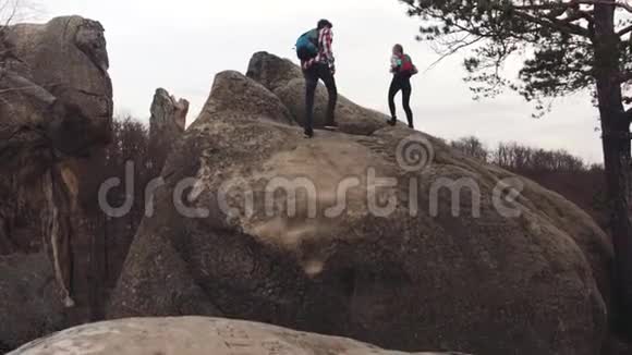 运动的男孩和女孩带着旅游背包爬上岩石山然后登上山顶牵着手视频的预览图