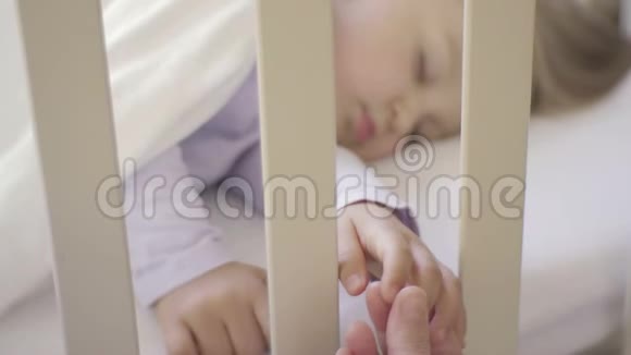父母握着睡在婴儿床上的小孩子的手幸福的家庭和她的新生儿在一起这就是视频的预览图