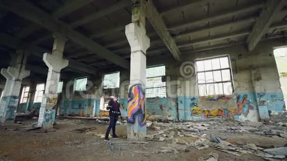 男式呼吸器涂鸦艺术家摇动喷漆然后在肮脏的空楼内的高柱上作画视频的预览图