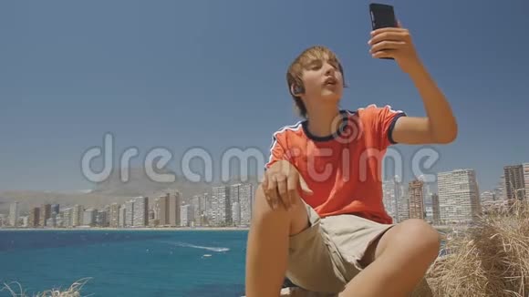 可爱的青少年男孩在智能手机上打视频电话展示海上城市天际线背景视频的预览图