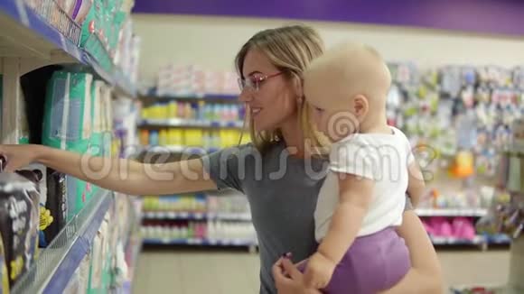 年轻漂亮的母亲戴着眼镜抱着她的孩子一边在挑尿布视频的预览图