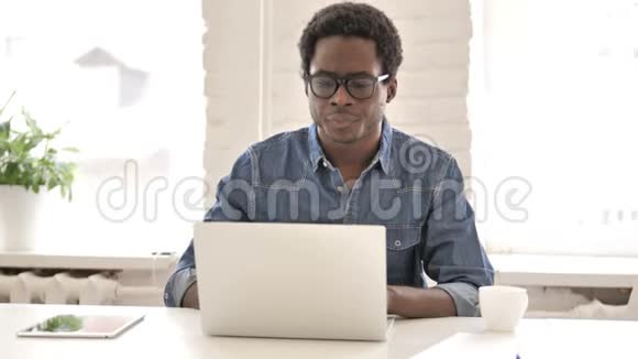 背部疼痛的非洲男人在手提电脑上工作视频的预览图