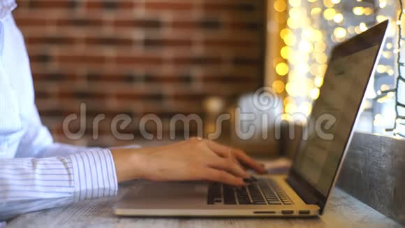 一张侧面照片拍摄的是一位年轻漂亮女子坐在咖啡厅的木桌旁忙着操作笔记本电脑的手视频的预览图