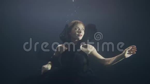 神秘的女人穿着黑色衣服像美人鱼一样在黑暗的游泳池里水下游泳视频的预览图