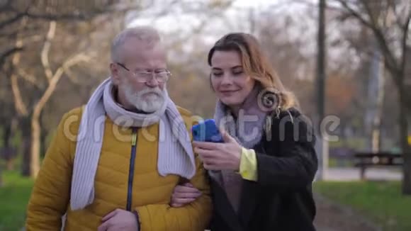 家庭自拍幸福的孙女和爷爷在公园散步时用手机拍照视频的预览图