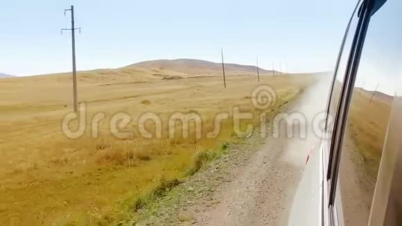 从窗户可以看到汽车在尘土飞扬的乡村道路上行驶有沙漠的田野和山丘视频的预览图