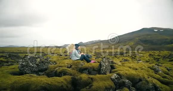鸟瞰年轻美丽的夫妇坐着欣赏冰岛熔岩场的景观直升机飞来飞去视频的预览图