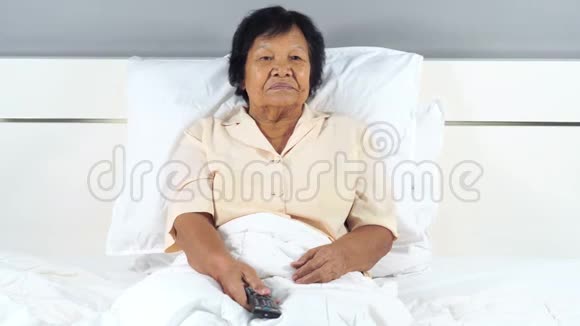 在床上用电视遥控器看恐怖电影的老妇人视频的预览图