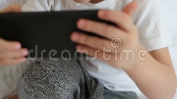 一个孩子拿着智能手机在他面前在白色背景下缓慢地玩游戏视频的预览图