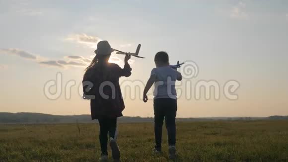 兄弟姐妹在日落时跑过田野玩飞行员孩子们玩木飞机童年视频的预览图