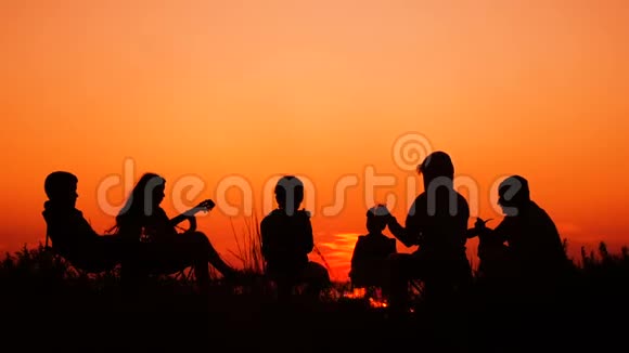 日落时分人们坐在海滩上篝火旁视频的预览图