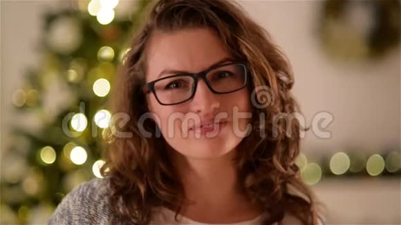 微笑的女人卷发戴着圣诞树背景上的眼镜漂亮的女孩看着相机微笑肖像视频的预览图