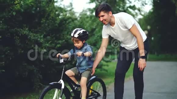 当他细心的父亲帮他拿着自行车教书时兴奋的男孩骑着自行车笑得很慢视频的预览图