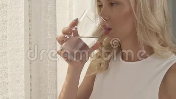 一个女人紧紧地抱着一杯水她的手摄像机向上移动一张漂亮金发脸的侧视图视频的预览图