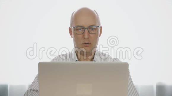 惊讶的成熟男人戴着眼镜看着笔记本电脑屏幕视频的预览图