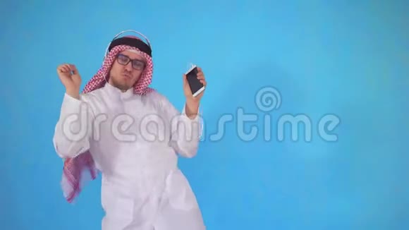 戴着耳机的阿拉伯男子站在蓝色背景上伴随着音乐翩翩起舞视频的预览图