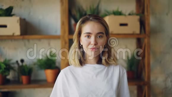 一个快乐的年轻女士看着镜头微笑着站在漂亮的现代公寓里的慢镜头肖像视频的预览图