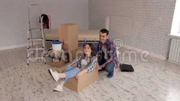 快乐夫妻在新公寓里玩得开心快乐女孩坐在纸板箱里视频的预览图