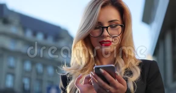 一位身穿正式服装戴着眼镜站在办公室外面用手机旋转的金发美女视频的预览图
