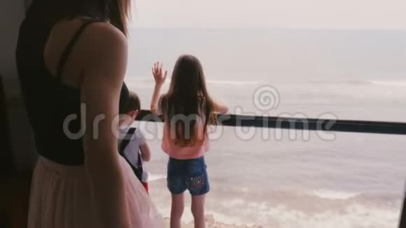 年轻的母亲和两个快乐兴奋的小孩子一起在大公寓的窗户上观看惊人的海景慢镜头视频的预览图