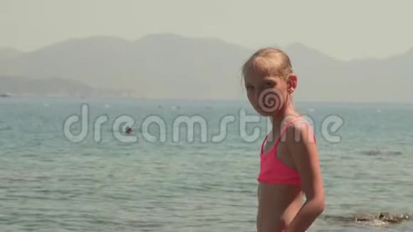 年轻的女孩穿着粉红色的泳衣在阳光明媚的海滩上看着大海的风景海山少女肖像画视频的预览图