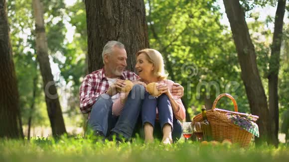 快乐的老夫妇在草地上休息吃汉堡在公园里浪漫约会视频的预览图