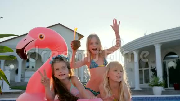 孩子们在暑假穿着泳衣的名人小女孩躺在游泳池附近的充气粉红火烈鸟上被宠坏的富人视频的预览图