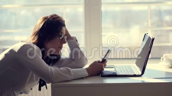 一位年轻的女职员办公室工作人员在上班的一间办公室里用手机浏览社交网络一小段视频的预览图