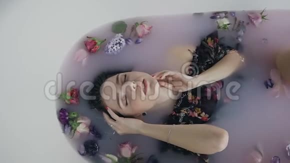 美丽的时尚模特女孩在奶浴中绽放芬芳的花蕾抚摸着脸上的皮肤水疗和护肤理念视频的预览图