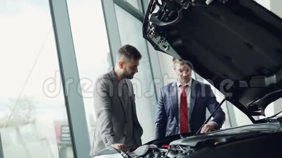 专业的汽车推销员在汽车引擎盖下演示客户汽车发动机男人们正在寻找汽车零部件视频的预览图