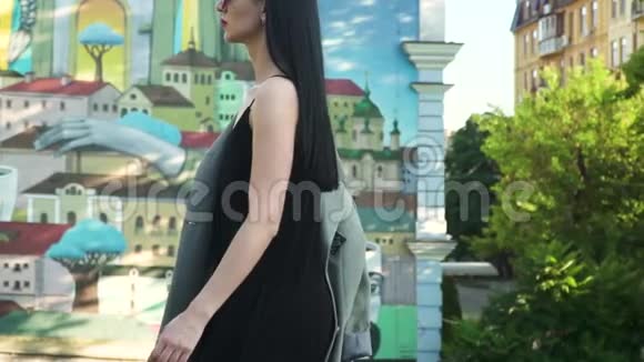 穿着黑色连衣裙和太阳镜的时尚女性在涂鸦中缓慢行走视频的预览图