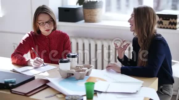 两位漂亮的经理妇女在休息时在现代办公桌上和咖啡聊天女老板听同事讲话视频的预览图