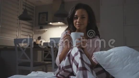 快乐的年轻女人穿着睡衣坐着茶巧克力咖啡杯微笑着视频的预览图