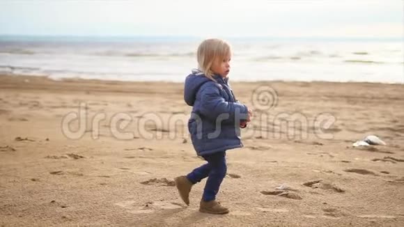 一个金发小男孩走在海边的沙滩上视频的预览图
