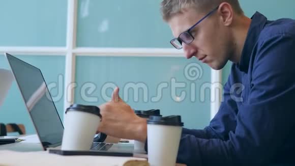 年轻的过度劳累或醉酒的商人打字在笔记本电脑键盘喝咖啡和睡着在办公室4K视频的预览图