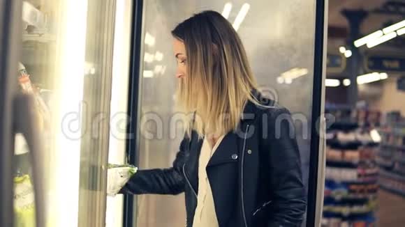 漂亮的女人在超市里选择冰箱里的乳制品年轻女人拿冷冻产品视频的预览图