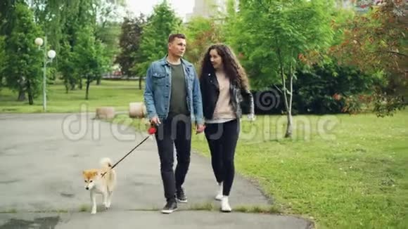 多莉拍摄的欢乐人群学生在城市公园遛狗盖伊牵着狗抱着他女朋友的视频的预览图