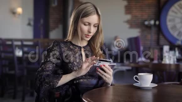 女士上网购买信用卡和智能手机坐在餐厅与人的背景穿黑色衣服的女人视频的预览图