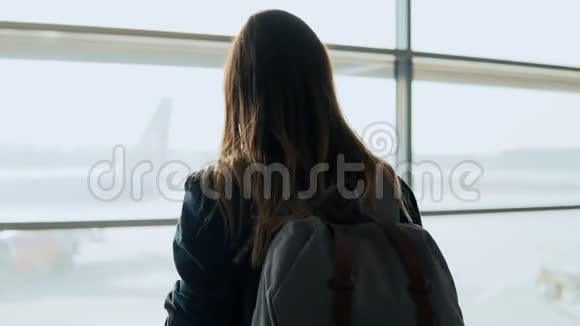在机场窗口附近使用智能手机的年轻女孩带背包的快乐欧洲女人在终端使用移动应用程序4K视频的预览图