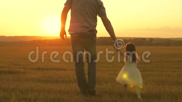 小女儿和她父亲牵着手在草地上散步孩子握着父亲手一家人晚上出去散步视频的预览图