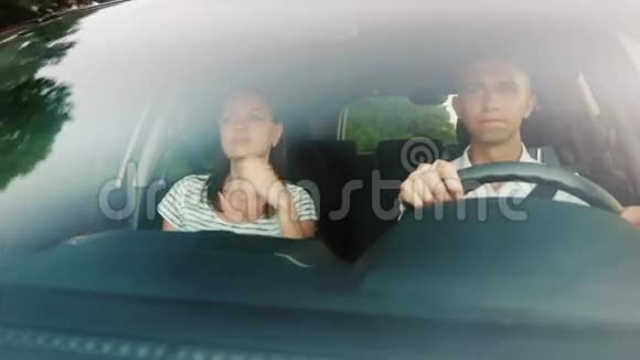 年轻夫妇在车里玩趣载歌载舞驾驶汽车时挡风玻璃反射树木和云层视频的预览图