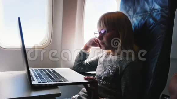 这个女孩6岁在飞机上飞行有点无聊想睡觉打哈欠在笔记本电脑上看动画片视频的预览图