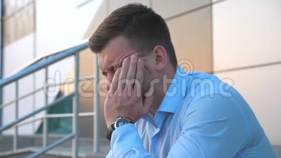 侧面看沮丧悲伤的商人坐在办公楼附近的楼梯上哭泣一个绝望的年轻人视频的预览图