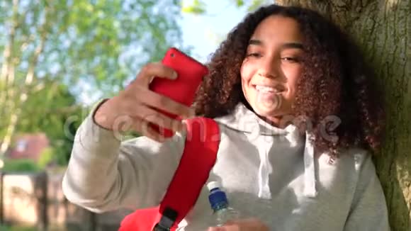 非裔美国少女在社交媒体上使用手机摄像头靠在树上视频的预览图