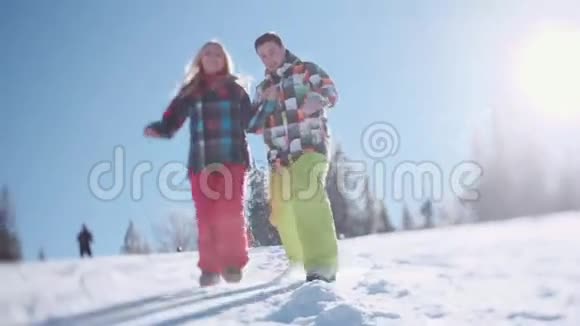 穿着五颜六色的滑雪服的幸福夫妇快乐的年轻人在雪地里滑向地面射击视频的预览图