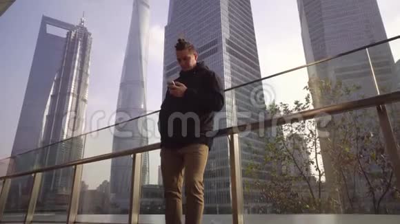 一个穿黑色夹克的年轻人在中国上海摩天大楼的背景上用电话视频的预览图