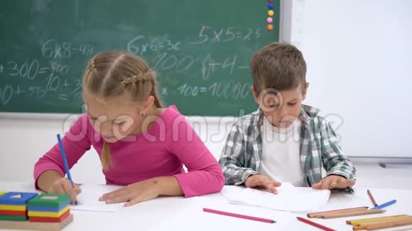 学校的爱同学在上课时在桌子上写字然后看镜头在黑板的背景上微笑视频的预览图