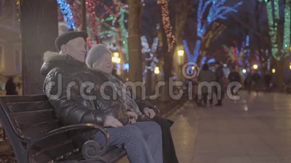 圣诞气氛中欢乐的孙儿童跑过来在圣诞气氛中的傍晚公园里爷爷奶奶坐在长凳上视频的预览图