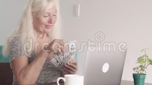 在家里坐在笔记本电脑前的时候一个退休的老奶奶的特写镜头显示了一捆钱视频的预览图